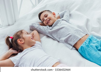 Two Sweet Kids Lying On Cozy Couch, Hands Over Head, Ready To Take A Nap.