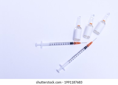 Two syringes placed on an isolated white background next to three glass vials with blank labels with room for text, top view.