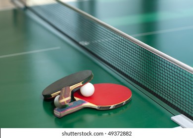 Two table tennis or ping pong rackets and balls on a green table with net; shallow DOF, focus on rackets