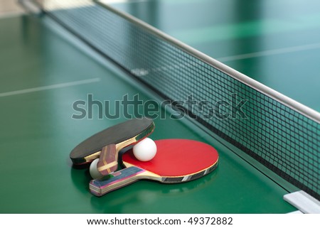 Two table tennis or ping pong rackets and balls on a green table with net; shallow DOF, focus on rackets
