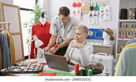 Two tailors, a man and a woman, collaborate in a colorful dressmaking studio filled with fashion design elements. - Powered by Shutterstock