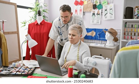 Two tailors, a man and a woman, collaborate in a colorful atelier surrounded by fashion design tools and garments. - Powered by Shutterstock