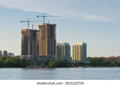 Two Tall Construction Cranes At The Site By The Lake. New Developments, Real Estate Bubble, Housing Crisis, Affordable Homes Concept.