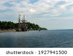 Two Tall Ships moored in a protected harbor near Brockville, Ontario on the St. Lawrence River with a treed shoreline in the background and a cloud filled blue sky