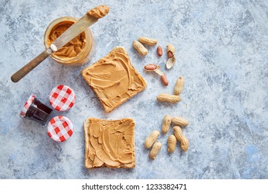 Two tasty peanut butter toasts placed on stone table. With small jars of fruit jam big peanut butter container. Knife on side. Above view with copy space - Powered by Shutterstock