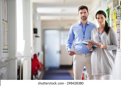 Two Teachers Standing In A School Corridor, They Are Both Dressed Smart Casual And Look Serious