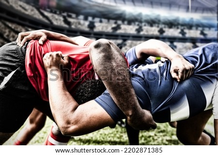 Two teams of multi-ethnic rugby players playing rugby at a sports stadium, wearing team strip, in a scrum, holding each other. Sport and competition concept digital composite.