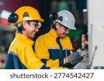 Two technicians inspect and operate a CNC machine in a metal workshop, checking controls and workflow during industrial production monitoring, maintenance and quality review.