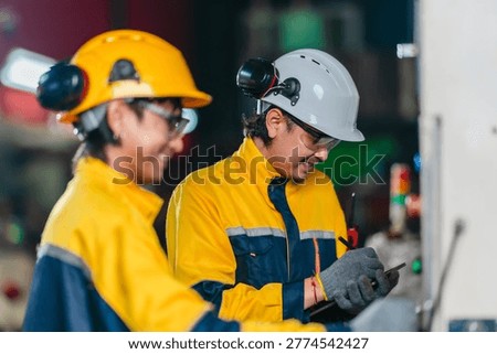 Two technicians inspect and operate a CNC machine in a metal workshop, checking controls and workflow during industrial production monitoring, maintenance and quality review.