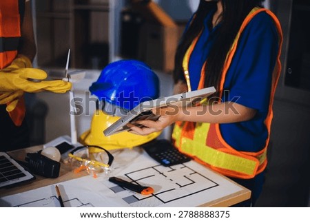 Two technicians inspect server racks in data center with tablet and fiber optic cable. Engineer and specialist discuss maintenance work in data center. Man and woman work together with safety equipmen