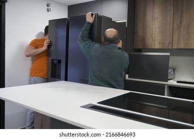 Two Technicians Installing An American Refrigerator In A New Modern Kitchen.