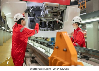 Two technicians in red overalls communicate via walkie-talkies while working on the coupling system of a train in a maintenance facility.