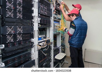 Two technicians switch fiber optic wires at the central router. Installers work in the data center server room. Maintenance of the hosting site.