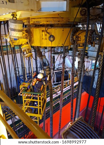 Two technicians working on a basket close to diverter of a drillship in moonpool area