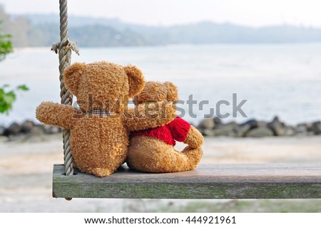 Two teddy bears sitting on the wooden swing with nature background. Concept about love and relationship.