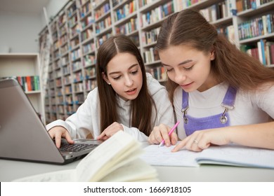 Two teen schoolgirls working on a project together at the library. Studying, learning concept - Powered by Shutterstock