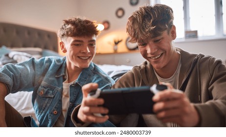 Two Teenage Boys At Home In Bedroom Together Playing On Handheld Computer Gaming Device Together - Powered by Shutterstock