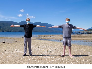 Two teenage boys standing at a beach showing social distancing using raised arms to show a two meter distance.