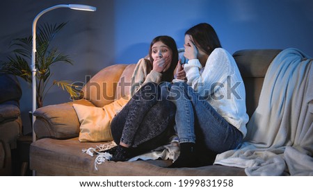 Two teenage girls closing eyes while watching scary horror show on TV at night