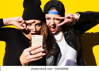 Two teenage girls friends in hipster outfit outdoors make selfie on a phone. 