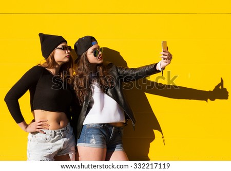Two teenage girls friends in hipster outfit outdoors make selfie on a phone. 