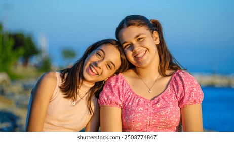 Two teenage girls friends, one slightly overweight and the other with dark skin, sitting on the rocks by the seaside, looking at the camera and smiling on a sunny summer day - Powered by Shutterstock