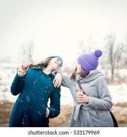 Two Teenage Girls Having Fun Outdoors On Snowy Winter Day In Park. Two Female Friends Enjoying Outside In Wintertime And Laughing.