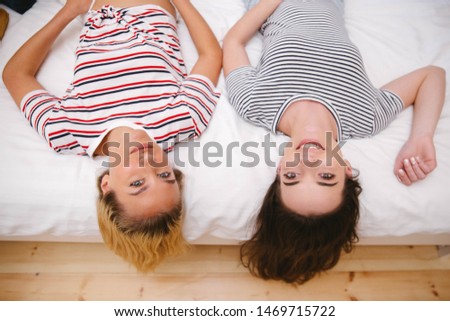 Two teenage girls lying on bed in cozy room and having fun.