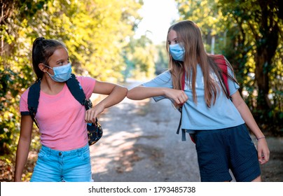 Two Teenage Girls say hello touching hands elbow meeting in the Park on the way to School. New handshake due to Coronavirus pandemic safety protective behavior