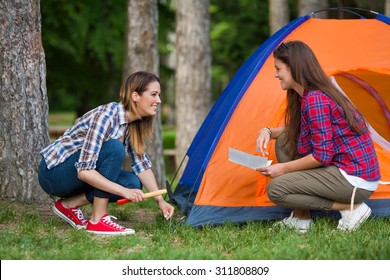 Two Teenage Girls Setting Up A Tent Following Instructions From The Handbook