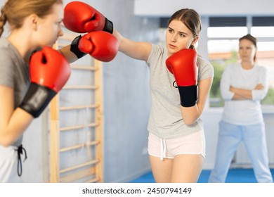 Two teenage girls in sportswear are engaged in boxing sparring in the gym under guidance of trainer in the gym - Powered by Shutterstock