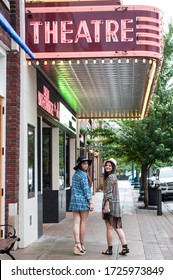 Two Teenage Girls Walking Down A Small Town Main Street By A Theater 