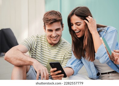 Two teenage happy friends watching funny videos browsing on internet app with a smartphone and smiling together. Caucasian couple using a cell phone to post in a social media and chatting online. High - Powered by Shutterstock