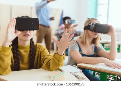 Two teenage schoolgirls using virtual reality headsets and classmate with teacher behind  - Powered by Shutterstock