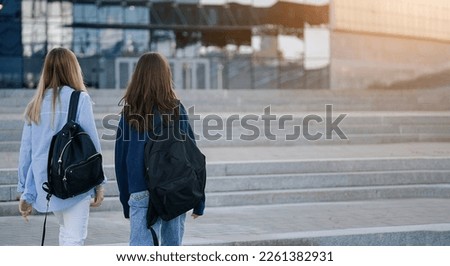 Two teenage student friends girls happy going to college or school. Back view	                              