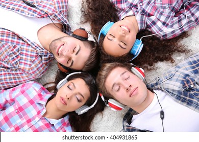 Two Teenager Couples Listening To Music With Headphones On A Carpet