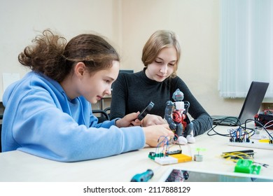 Two teenager girl at robotics school makes robot managed from the constructor, children learn robot constructing.