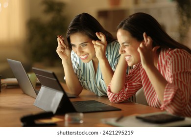 Two tele workers crossing fingers waiting for online result checking laptop in the night - Powered by Shutterstock