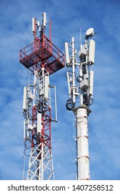Two telecom cellular base station towers at blue sky with clouds
