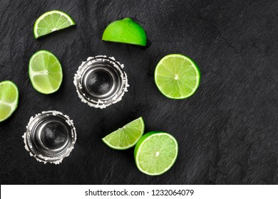 Two tequila shots with lime slices and wedges, shot from the top on a dark background with a place for text - Powered by Shutterstock