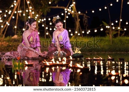 Two thai woman holding a krathong sitting on a raft by the river, Asian women in traditional Thai costumes bring krathongs to float on Loi Krathong Day, traditions and culture of Thailand,