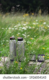 Two thermos for tea in nature on a background of green grass. A couple of tourists resting in nature with herbal tea.