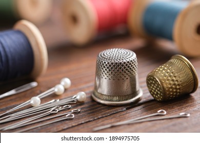Two thimbles and including pins. Various wooden spools of multicolored threads on background.