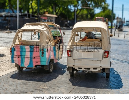 Two three-wheeled tourist Tuk tuks parked on a cobblestone street in Lisbon, Portugal, with tram tracks on the ground.