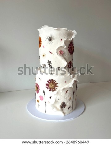 Two tier wedding cake with pressed flower decorations. Iced in a textured white wraparound fondant with colourful fresh pressed flowers