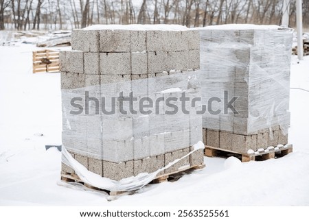 Two tightly wrapped pallets of bricks are sitting immobile in the cold, fluffy snow, standing out in stark contrast against the beautiful wintry landscape that surrounds them entirely