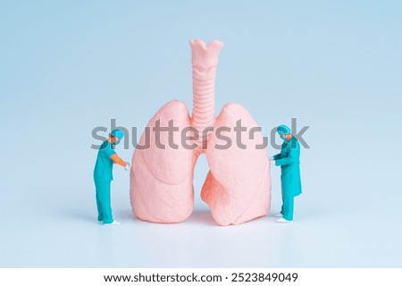 Two tiny surgeons examining a large pink lung model, symbolizing medical practices and healthcare advancements.