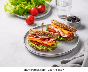 Two toast club sandwiches made of grain bread with cheddar cheese and bacon stuffed with tomatoes and lettuce and arugula on a light background with olives and glass of water.  - Powered by Shutterstock