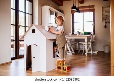 Two toddler children playing with a carton paper house indoors at home.