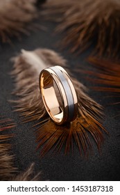 Two tone gold wedding ring on black background with feathers. Silver and gold male wedding ring band